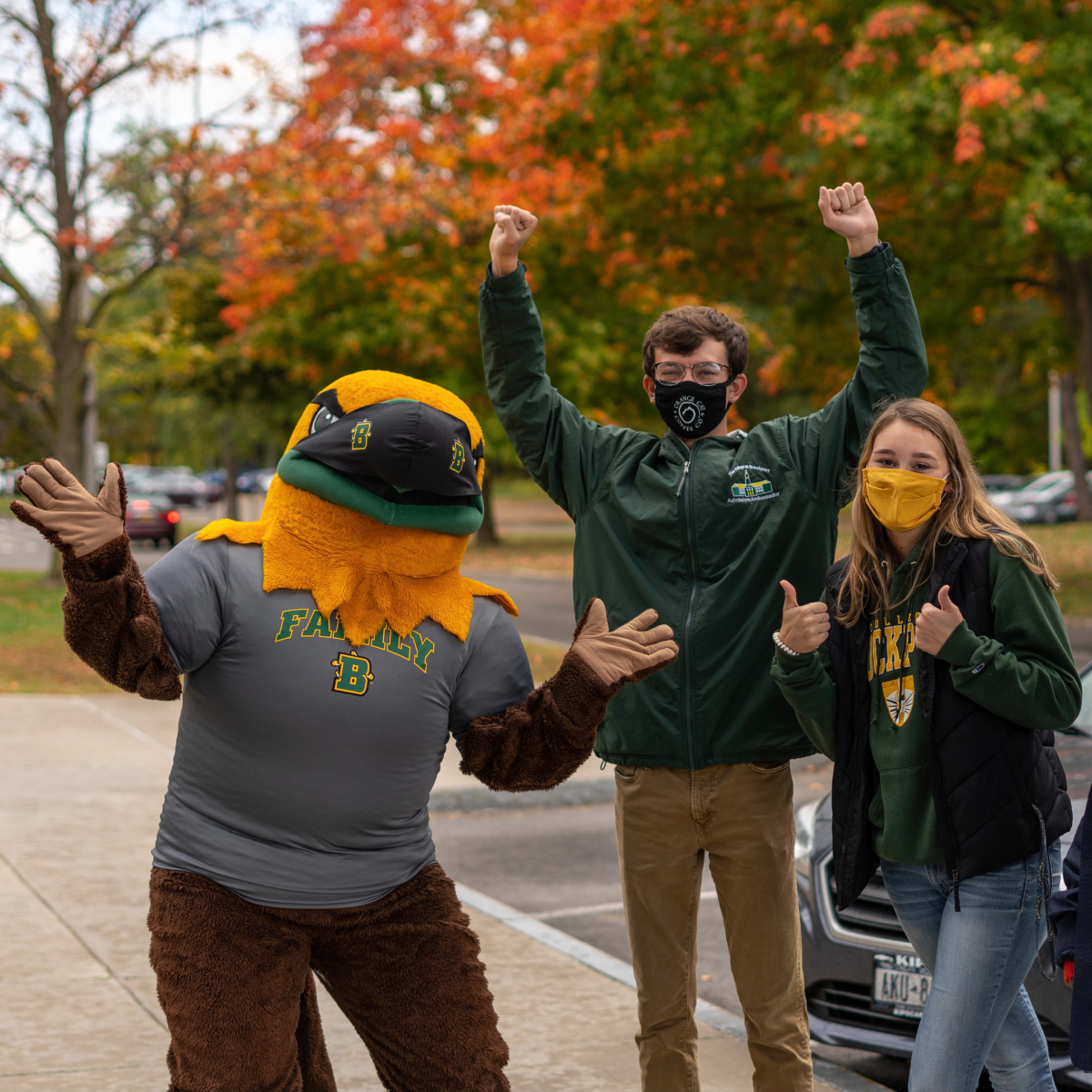 Ellsworth and two students, wearing masks, with a fall scene behind them